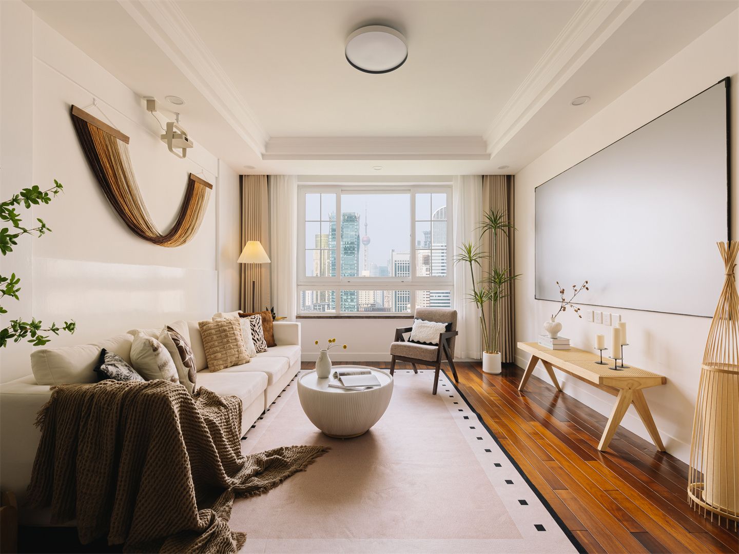 A modern living room with a sofa, armchair, coffee table, and a view of the city through large windows.