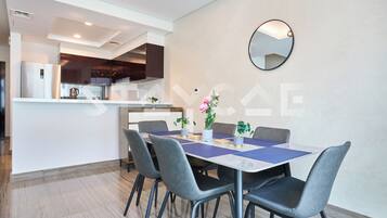 A modern dining area with a rectangular table, four grey chairs, and a round mirror on the wall.