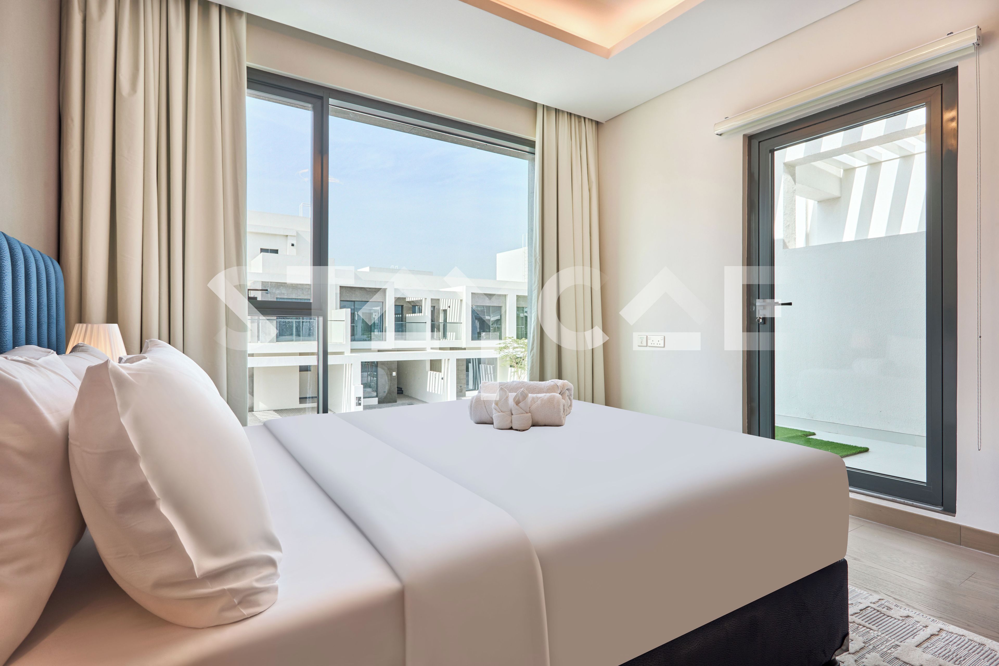 A hotel room with a bed, curtains, a view of buildings, and a sliding door.