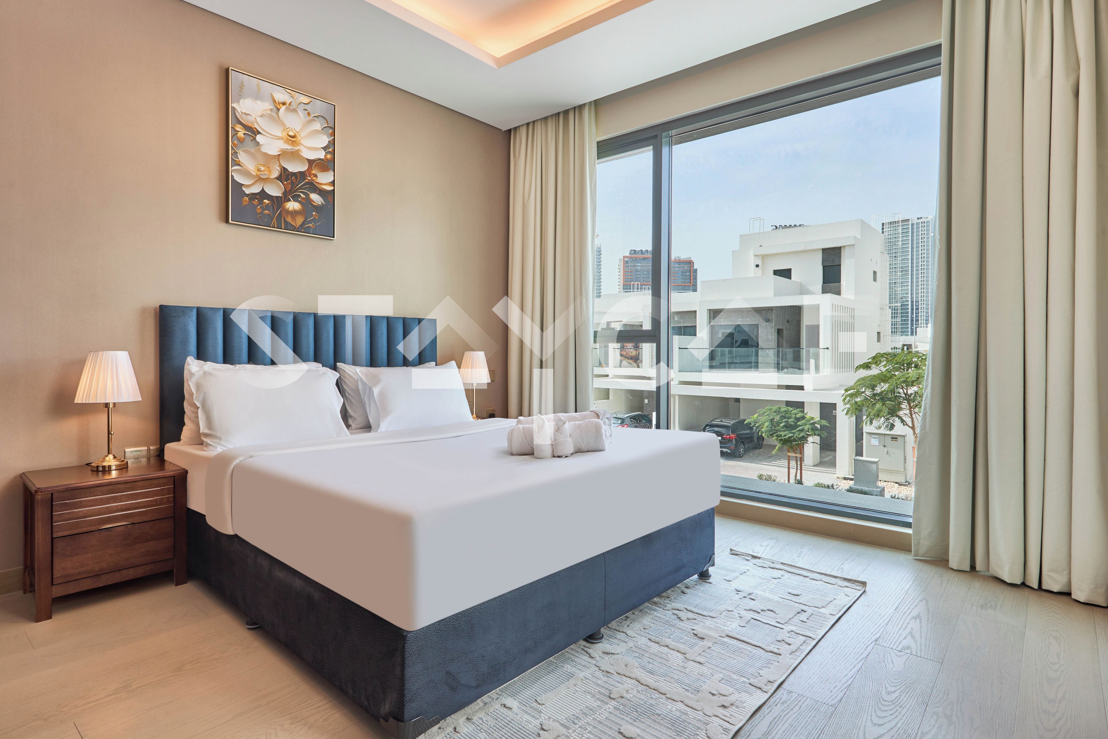 Una habitación de hotel moderna con una cama grande, una mesita de noche, dos lámparas, vistas de la ciudad a través de amplias ventanas y un cuadro en la pared.