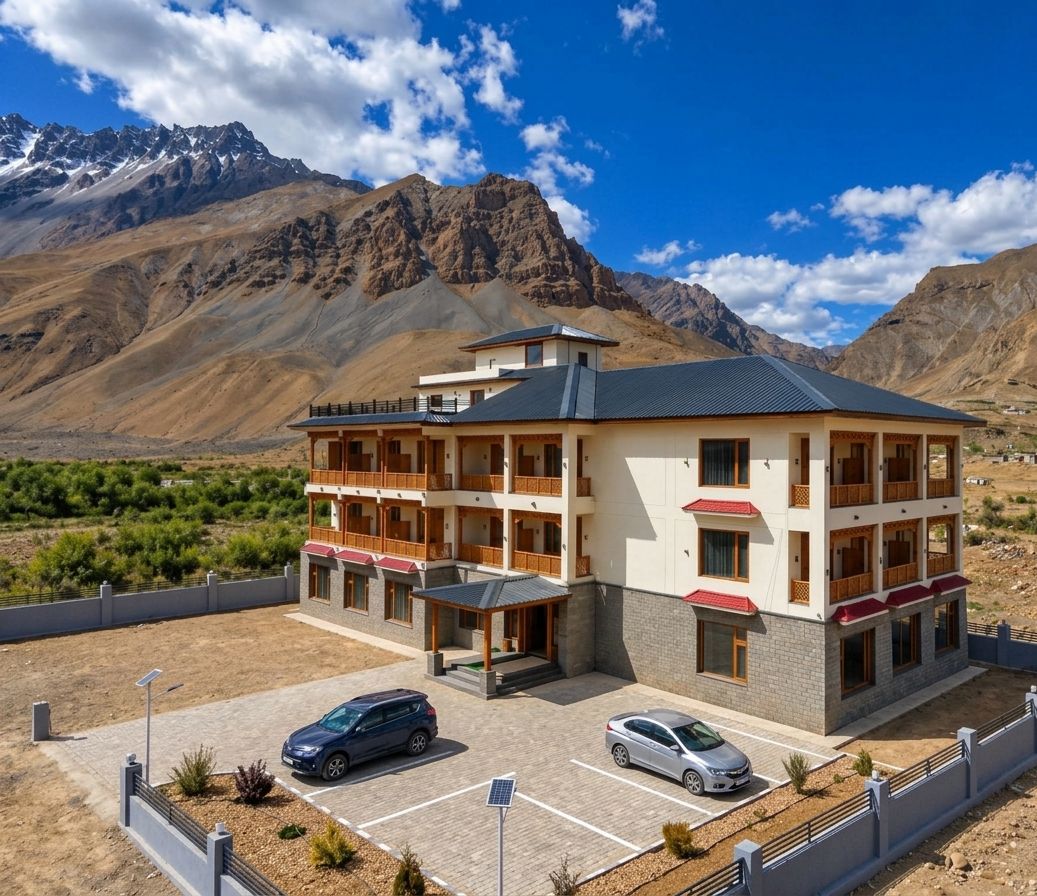 Un hotel de diverses plantes amb balcons, una zona d'aparcament i un paisatge de muntanyes al fons.