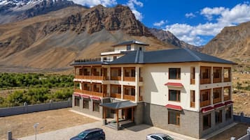 A multi-story hotel with balconies, a parking area, and a mountainous backdrop.