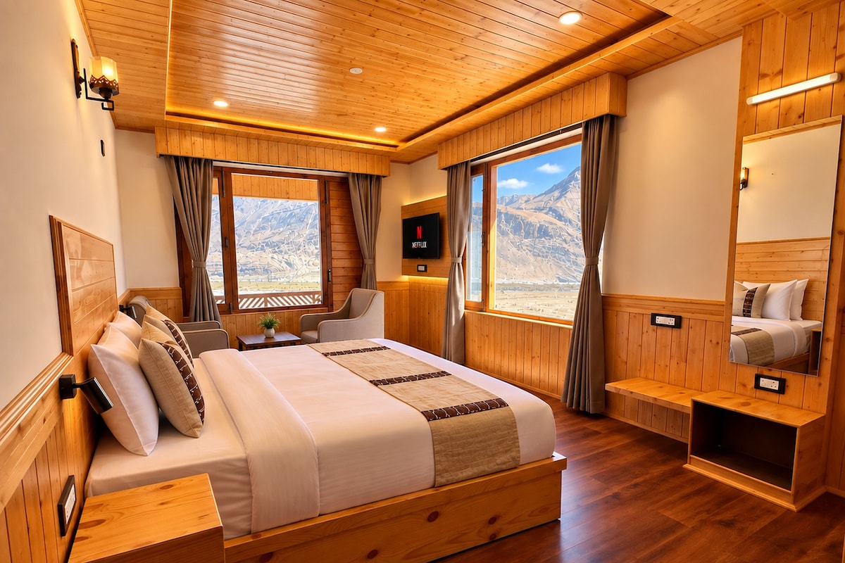 Camera da letto con rivestimento in legno, un letto, comodini, una TV e vista sulle montagne.
