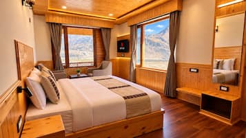 A wooden-paneled bedroom with a bed, bedside tables, a TV, and a view of mountains.