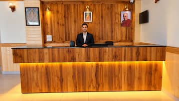 A reception desk with a wooden finish, a seated individual, and framed pictures on the wall.