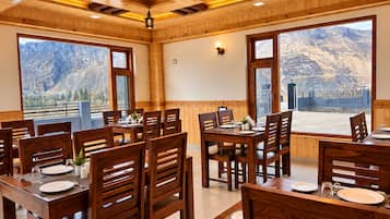 A restaurant with wooden interiors, large windows with mountain views, and a high ceiling with exposed beams.