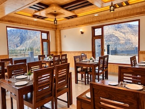 Un ristorante con interni in legno, ampie finestre vista montagna e un soffitto alto con travi a vista.
