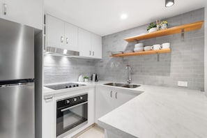 A modern kitchen with stainless steel appliances, white cabinetry, and grey tiled backsplash. - Coastal Escape - Short & Extended Stays (Surfers Paradise)