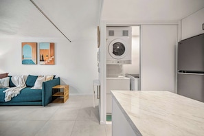 A modern kitchen with a built-in washer and dryer, a teal sofa with cushions, and a marble countertop. - Coastal Escape - Short & Extended Stays (Surfers Paradise)