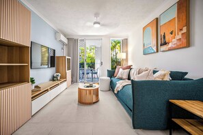 A modern living room with a sofa, a coffee table, and a TV mounted on the wall. - Coastal Escape - Short & Extended Stays (Surfers Paradise)