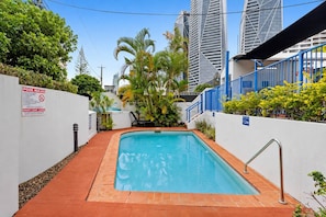 A rectangular pool with a metal ladder, surrounded by white walls and a red brick pathway. - Coastal Escape - Short & Extended Stays (Surfers Paradise)