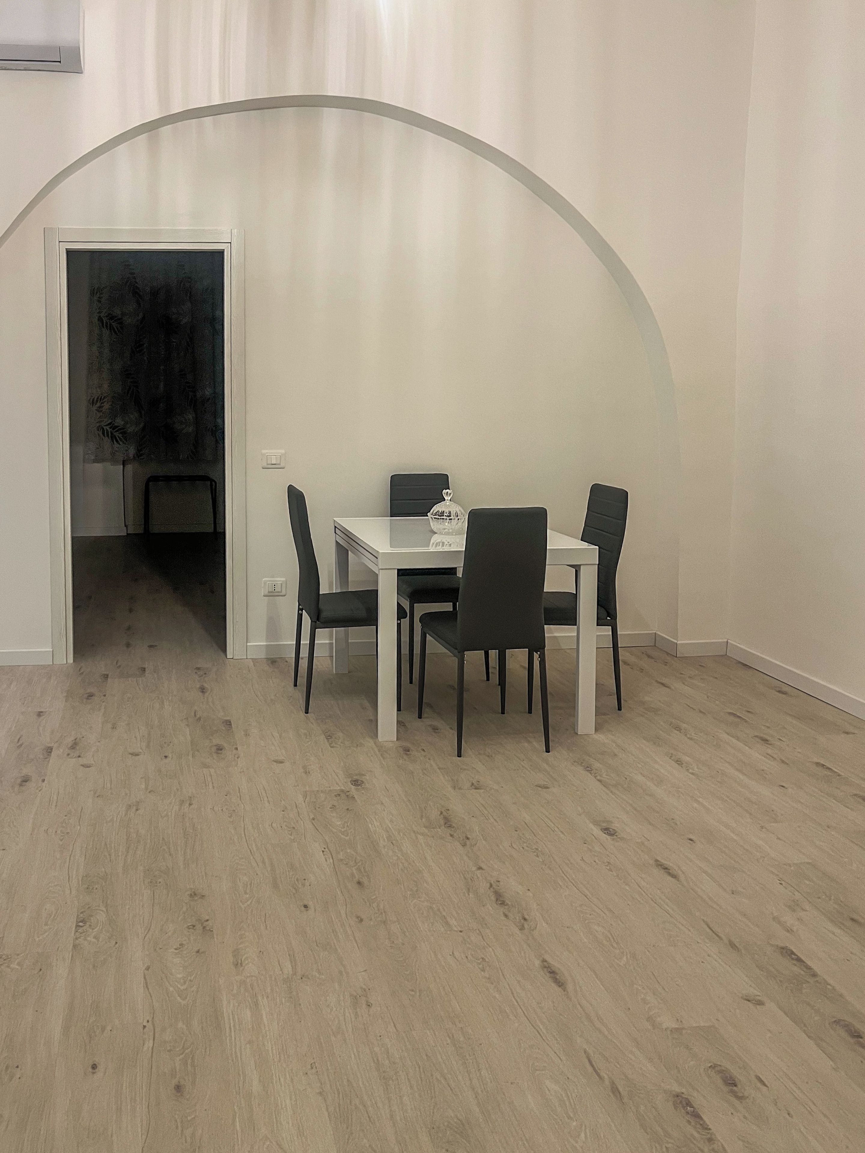 A dining area with a white table and four chairs, a glass cabinet, and a door leading to another room.