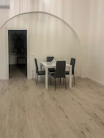 Un comedor con una mesa blanca y cuatro sillas, un aparador de vidrio y una puerta que da a otra habitación.