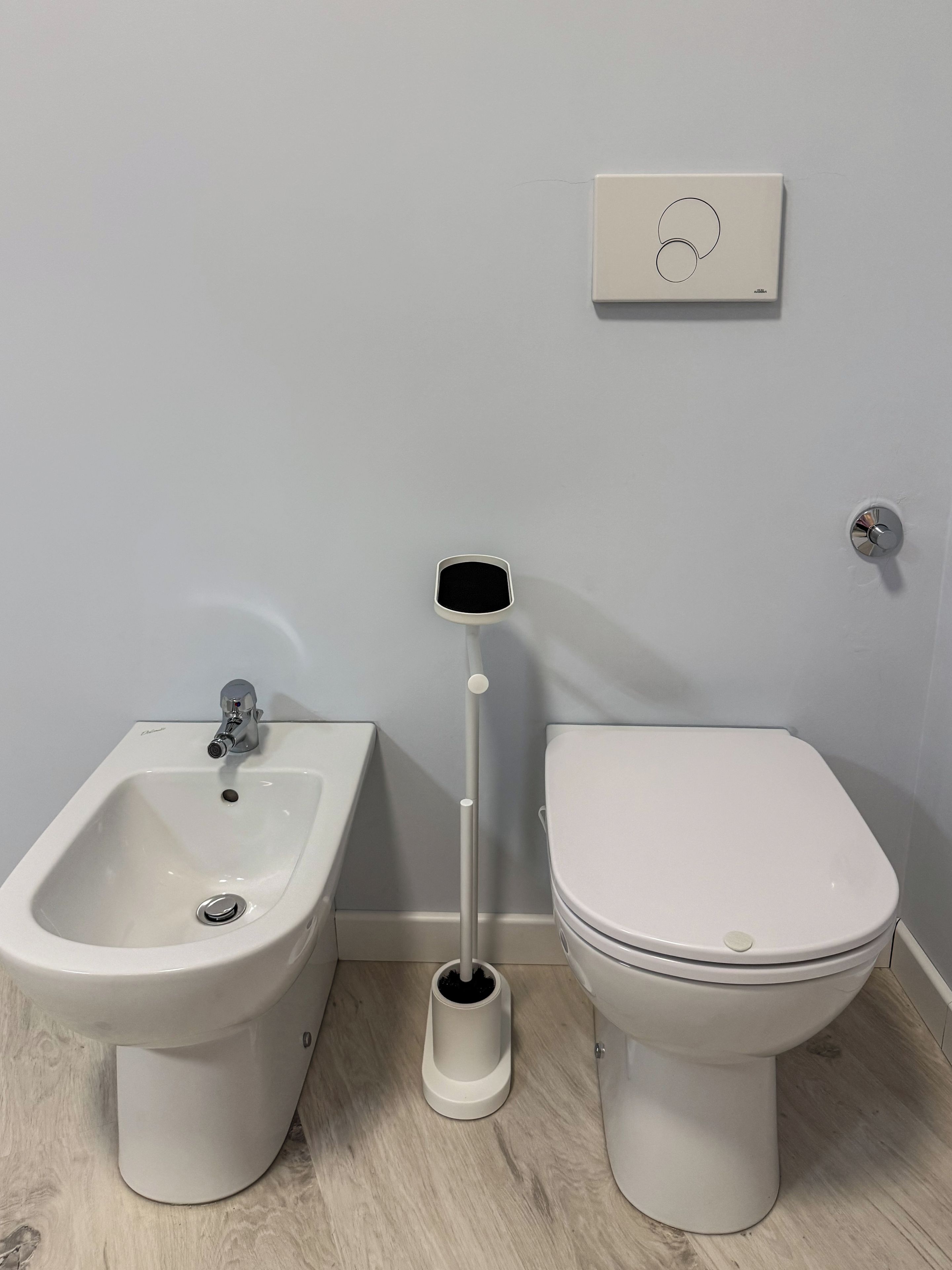 Ein Badezimmer mit einer Bidet-Funktion, einer Toilette und einem Wand-Spülknopf.