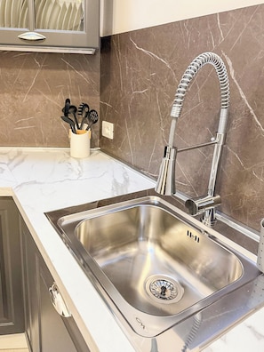Una cocina con un lavamanos de acero inoxidable, un grifo flexible y un protector contra salpicaduras de mármol.