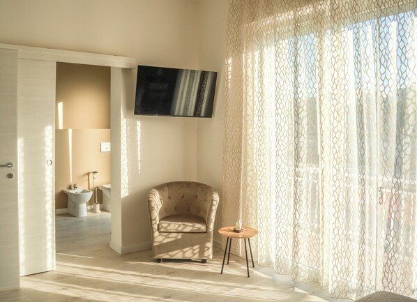 A room with a beige armchair, a small wooden table, and a TV mounted on the wall.