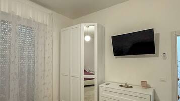 A bedroom with a wardrobe, a dresser, a television, and a bed with a red blanket.
