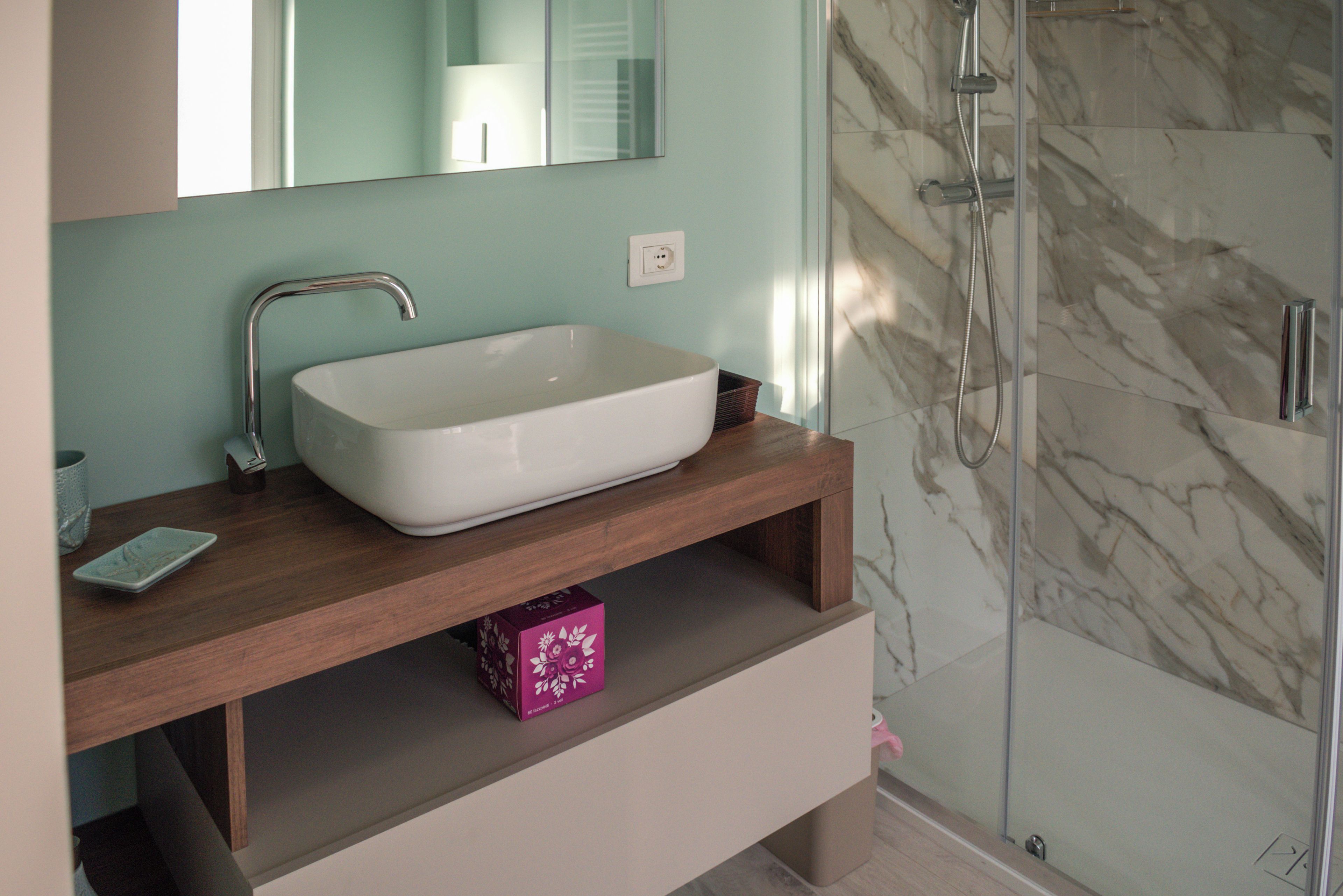 A bathroom with a white sink, a mirror, a shower, and a marble wall.