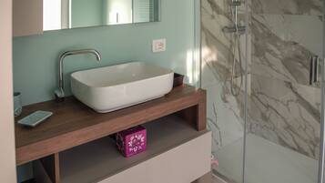 A bathroom with a white sink, a mirror, a shower, and a marble wall.