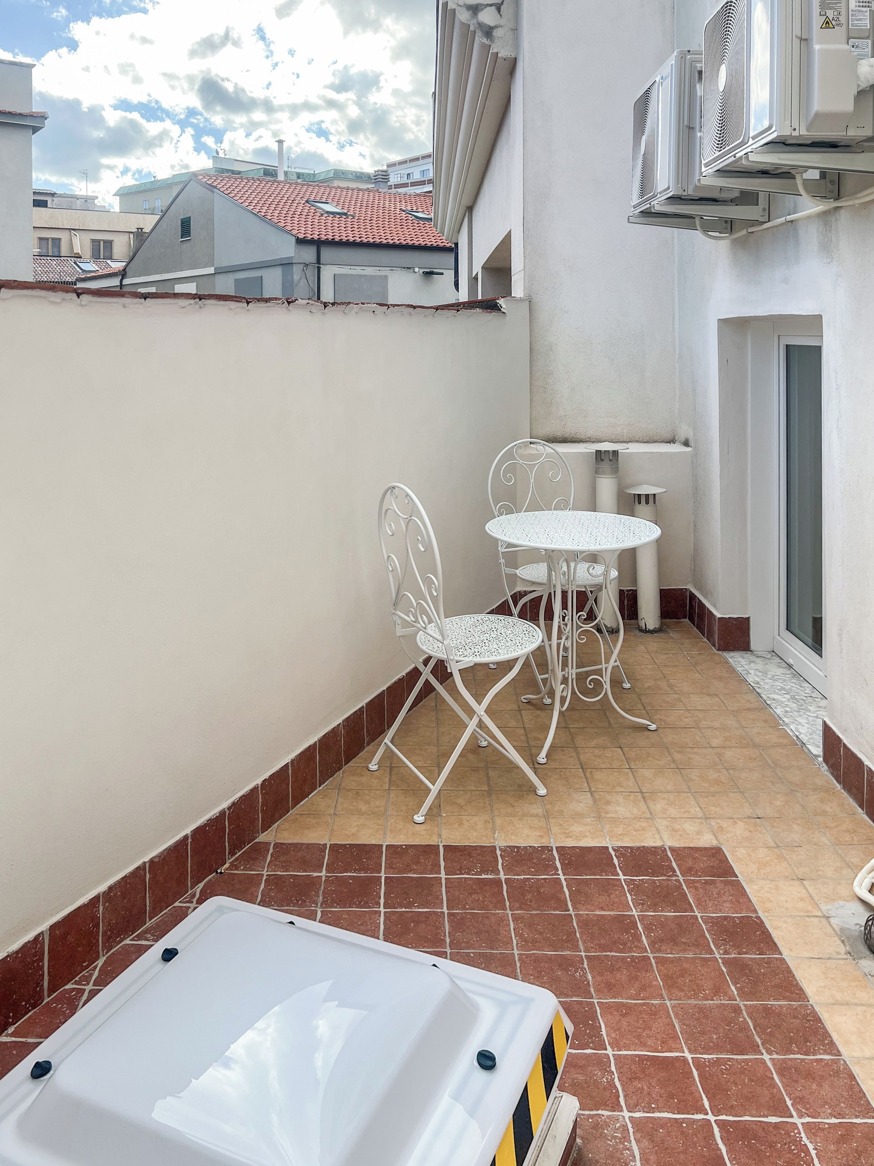 A small outdoor patio with a white table and chairs, a white bathtub, and a tiled floor.