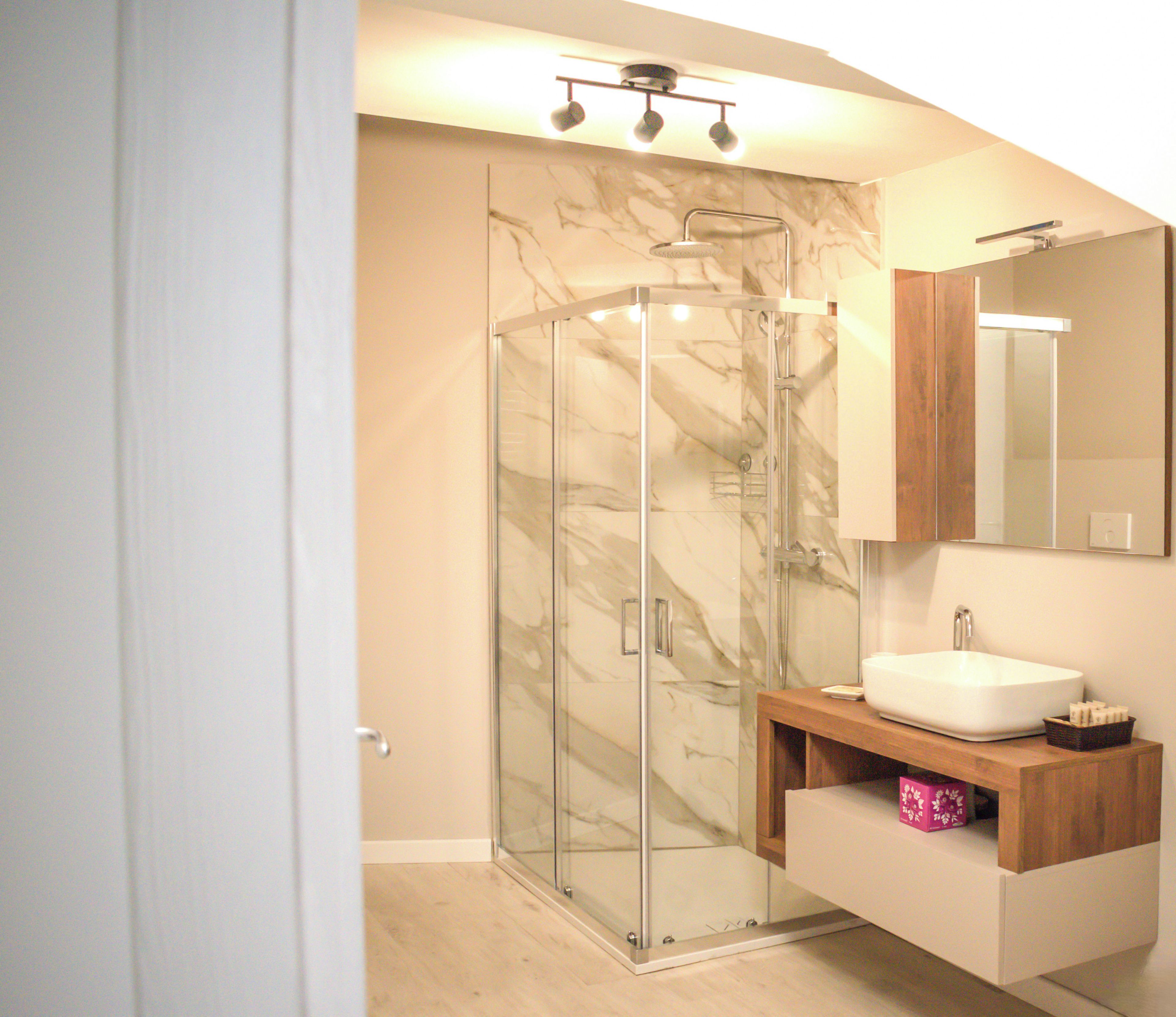Ein modernes Badezimmer mit einer gläsernen Dusche, einem weißen Waschbecken und einem Holztischchen.