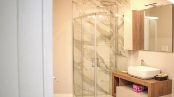 Ein modernes Badezimmer mit einer gläsernen Dusche, einem weißen Waschbecken und einem Holztischchen.