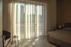 Un dormitorio con cama, una silla, una mesita y una ventana con cortinas estampadas.