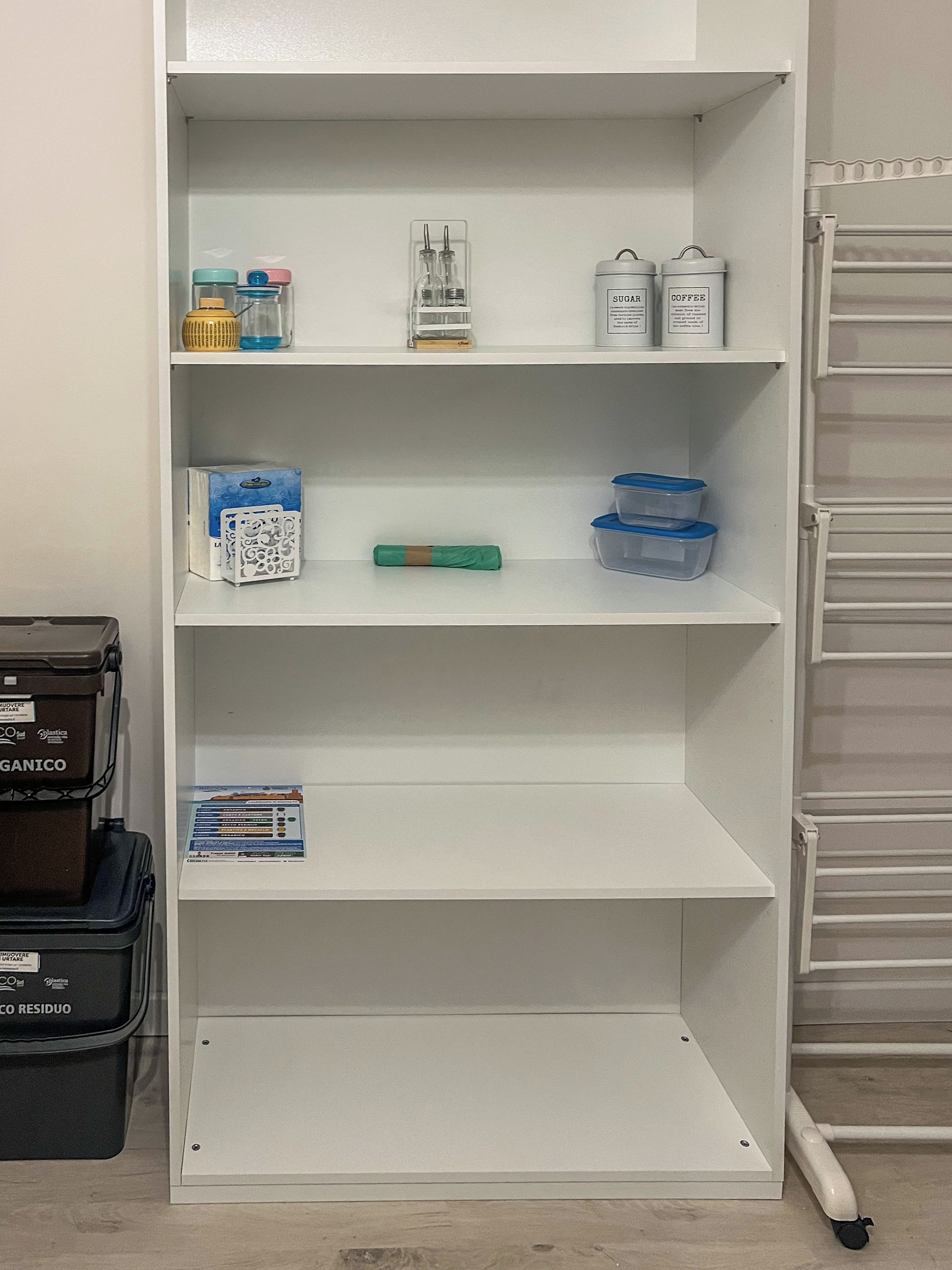 A white shelving unit with various storage containers and items, including a box labeled 'CO RESIDUO' and a blue container.