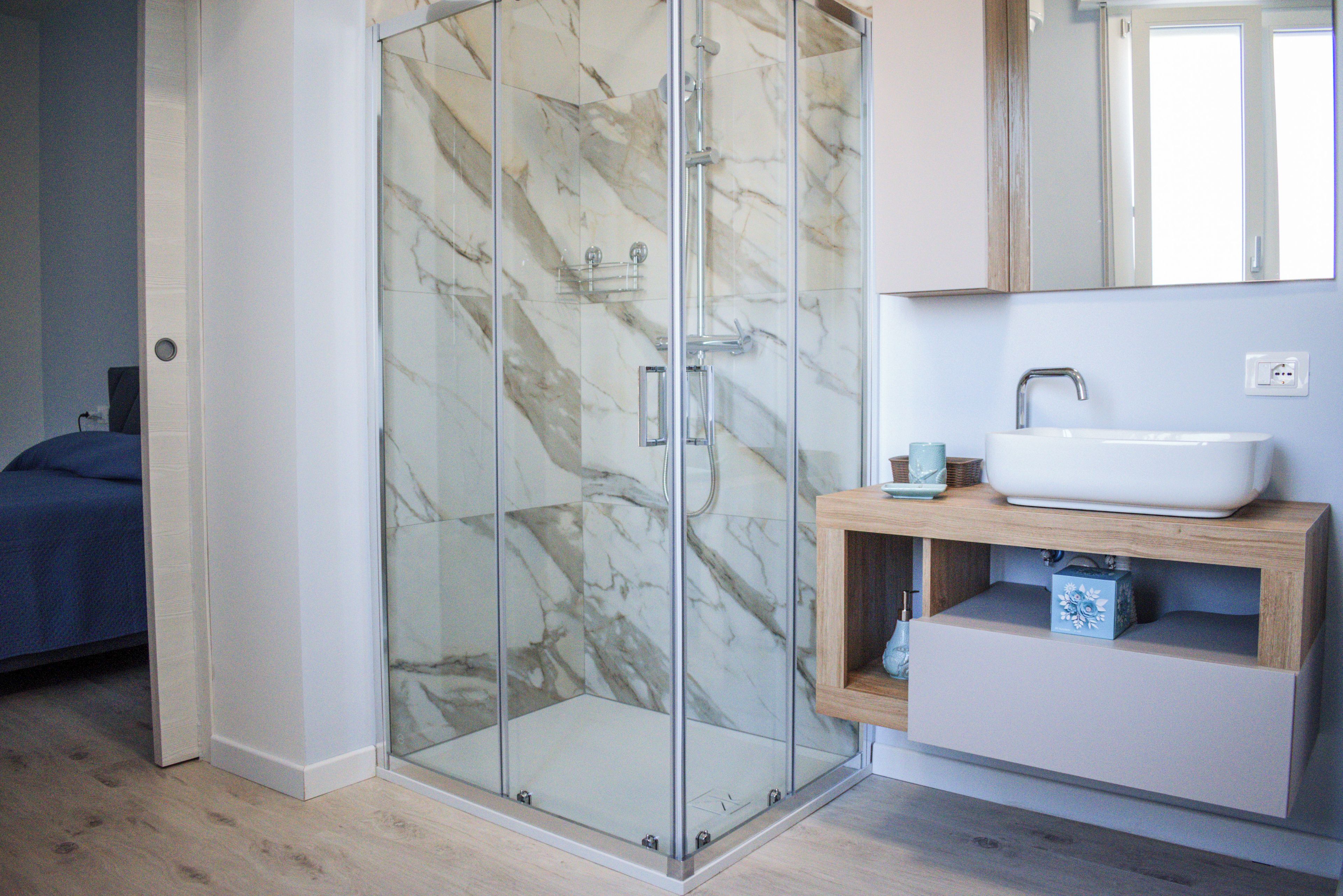 Un baño moderno con cabina de ducha de vidrio, un lavabo blanco y un mueble de tocador de madera.