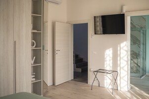 Una habitación con piso de madera, una puerta blanca, una mesita pequeña y un televisor montado en la pared.