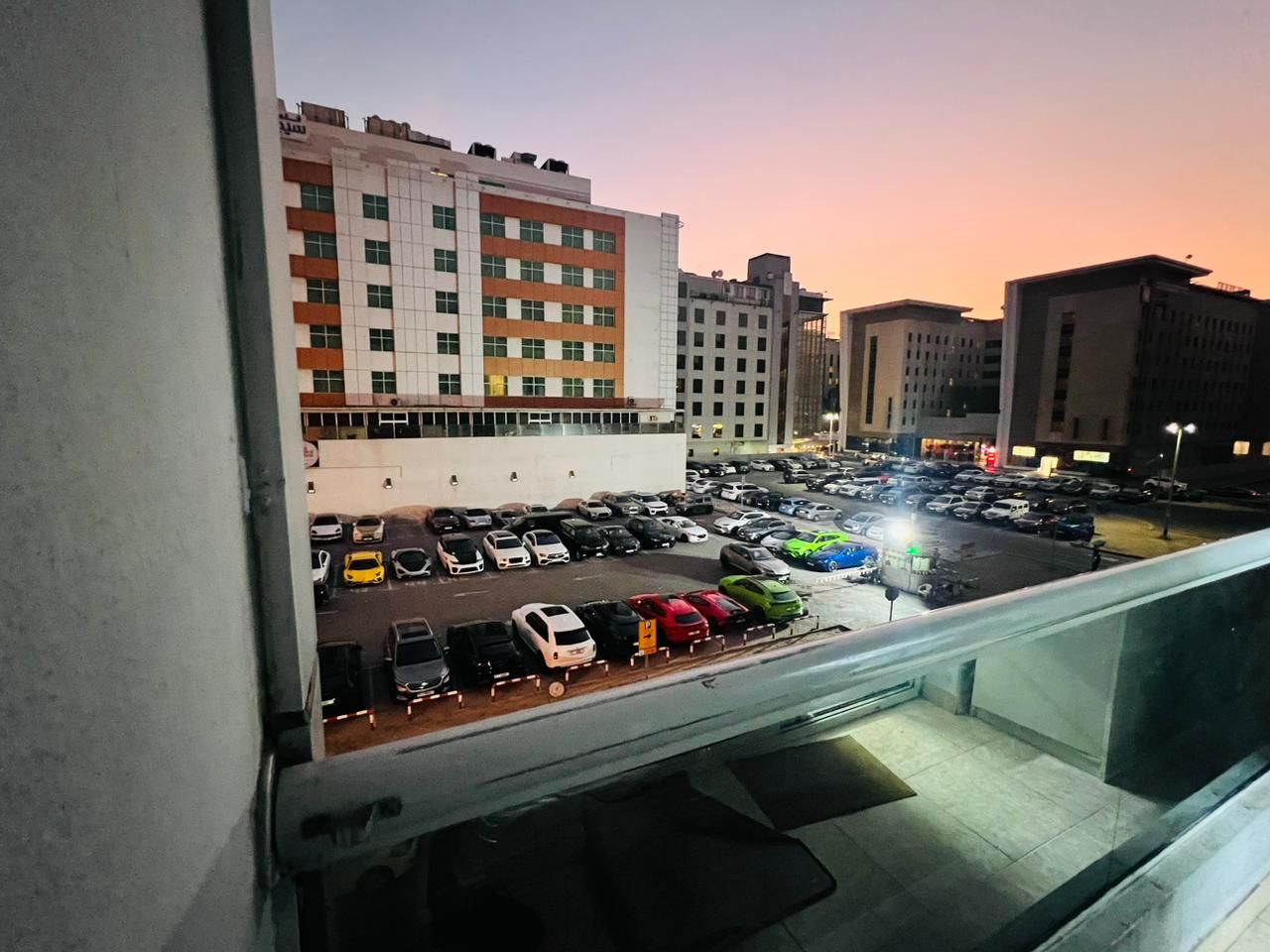 A parking lot with various vehicles, including cars and a truck, and a building with multiple floors in the background.