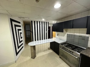 A kitchen with a gas stove, black cabinets, and a white countertop. - Fancy Partition Room in Al Barsha1 (Dubai)