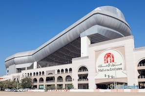 A modern architectural building with a prominent curved roof and a sign indicating it is the Mall of the Emirates.