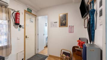 Ett hotellrum med en brandsläckare, en dörr med en nödutgångsskylt, en inramad tavla på väggen, en tv och ett blått paraply.