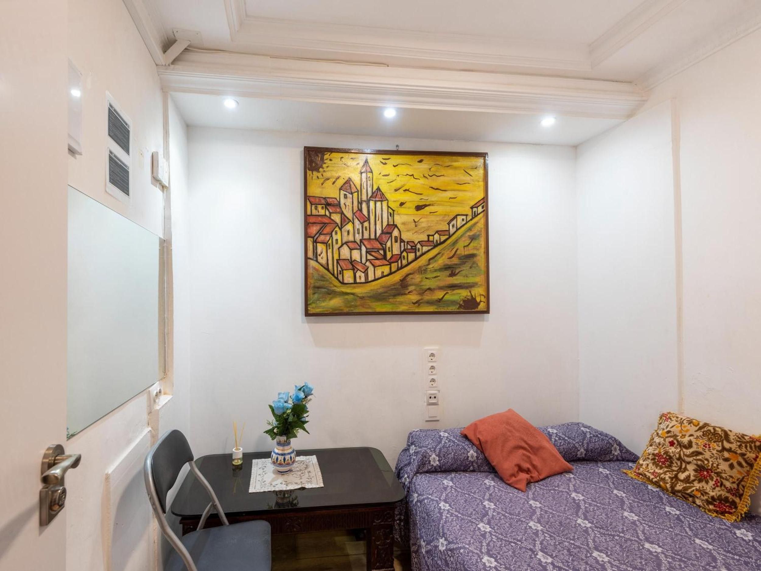 Una stanza con un letto, una scrivania e un quadro che raffigura un panorama urbano.