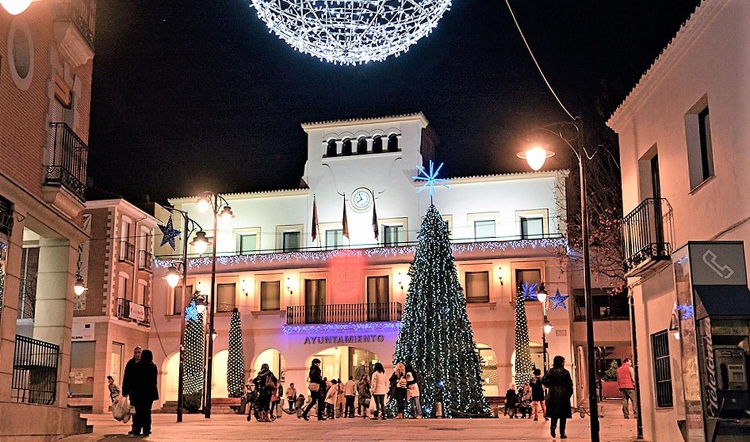 Un edificio con una torre dell'orologio, un albero di Natale e persone che passeggiano di fronte.
