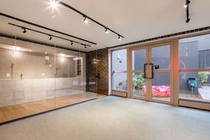 Un baño moderno con puertas de ducha de vidrio, pared con azulejos y zona exterior visible a través de las puertas de vidrio.