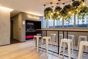 Un moderno café con un letrero que dice '¡Tómate un Respiro! Es Hora del Café' y vistas de la ciudad a través de amplias ventanas.