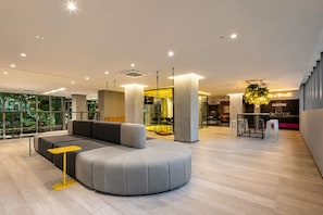 A modern interior with a curved grey sofa, a yellow table, and a coffee shop area with a sign that reads 'Coffee Break'. - On Paulista 817 (Vila Mariana)