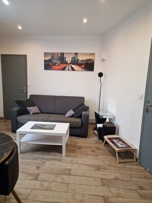 A living room with a grey sofa, a white coffee table, a black floor lamp, and a cityscape painting on the wall. - Vrbo Property (Nanterre)
