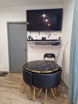 A dining area with a round table, chairs, a television mounted on the wall, and a shelf with electronic devices. - Vrbo Property (Nanterre)