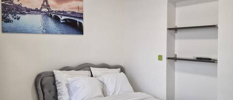 A bedroom with a bed, a desk, and a wall-mounted shelf unit.
