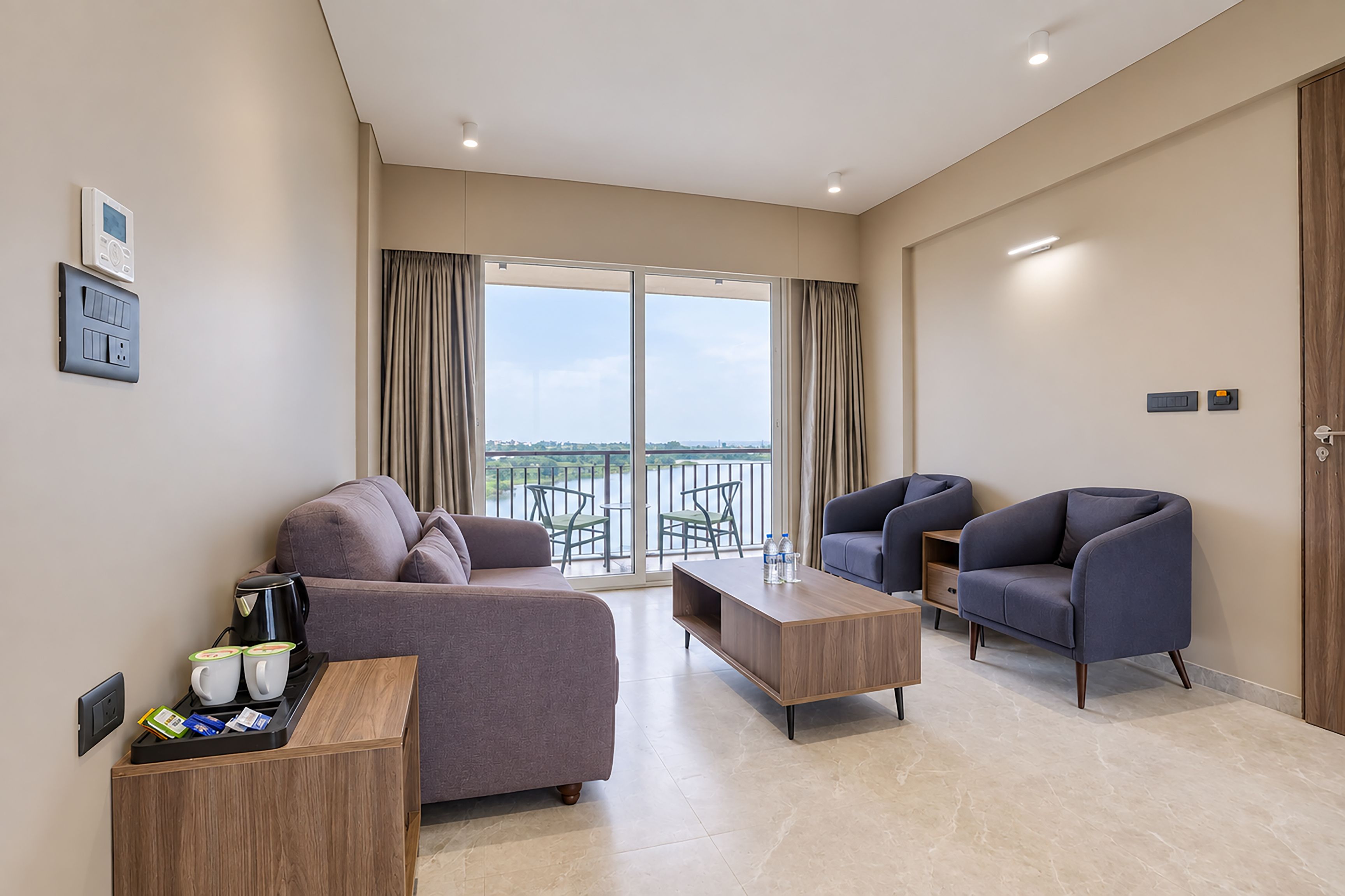 A modern living room with a sofa, two armchairs, a coffee table, and a balcony with a view.