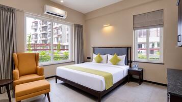 Quarto de hotel com cama, cadeira, mesa de cabeceira e janela com vista para um edifício.