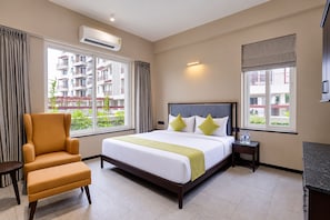 A hotel room with a bed, a chair, a nightstand, and a window with a view of a building. - The Byke Luxe Astara (Nashik)