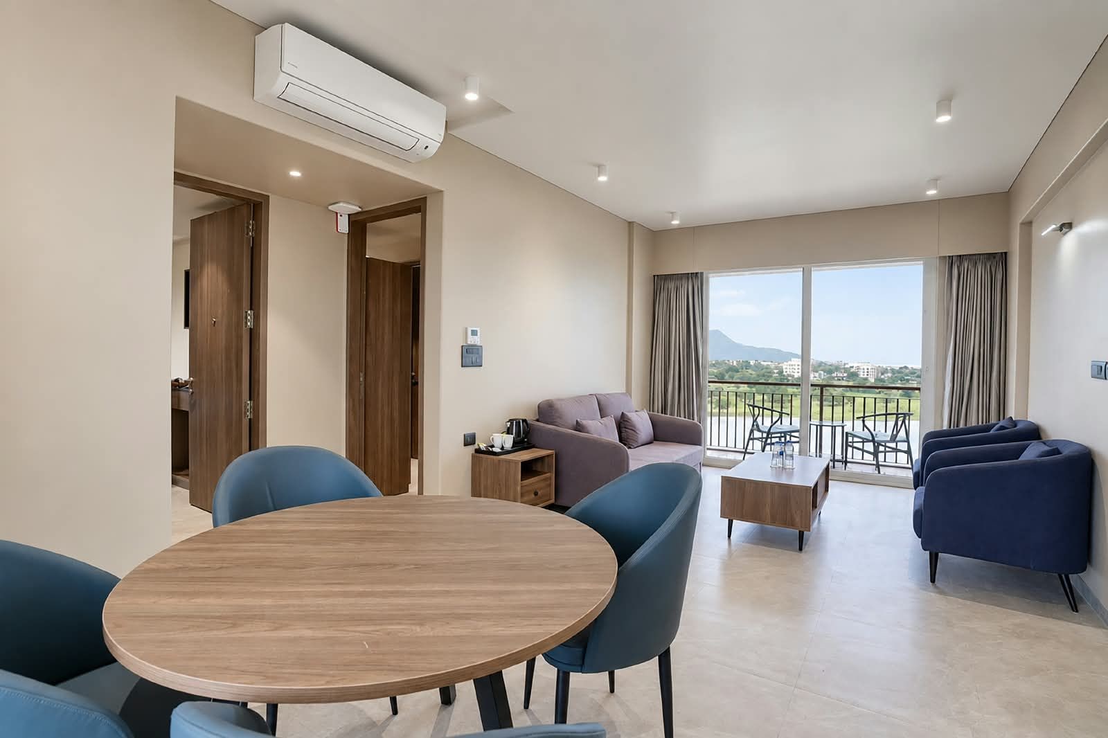 Una sala de estar moderna con una mesa redonda de madera, sillas azules, un sofá y un balcón con vistas.
