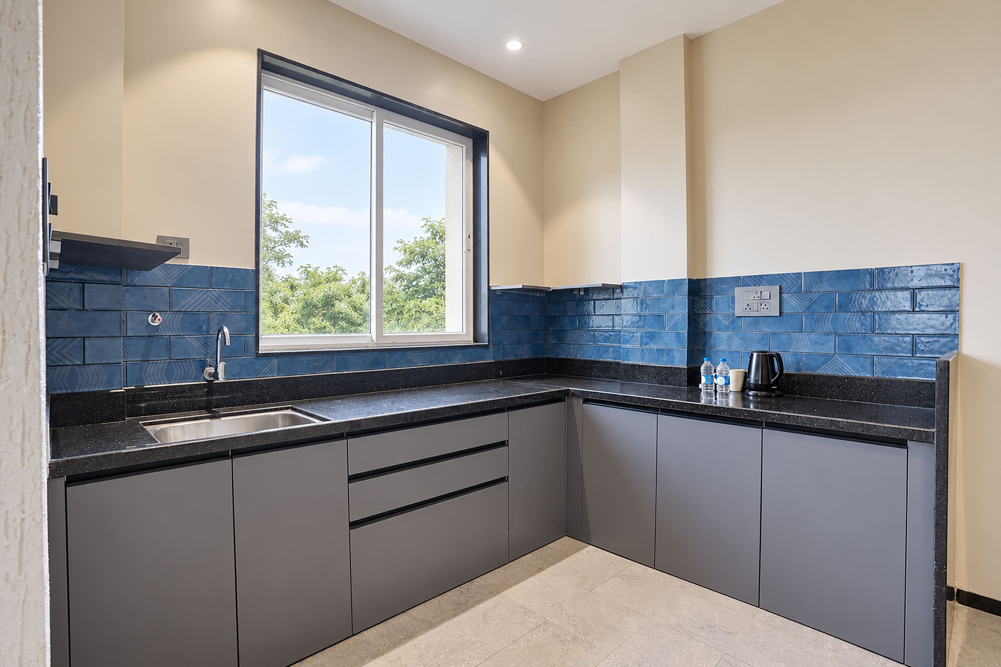 A kitchen with a window, dark grey cabinets, a black countertop, and blue patterned backsplash.