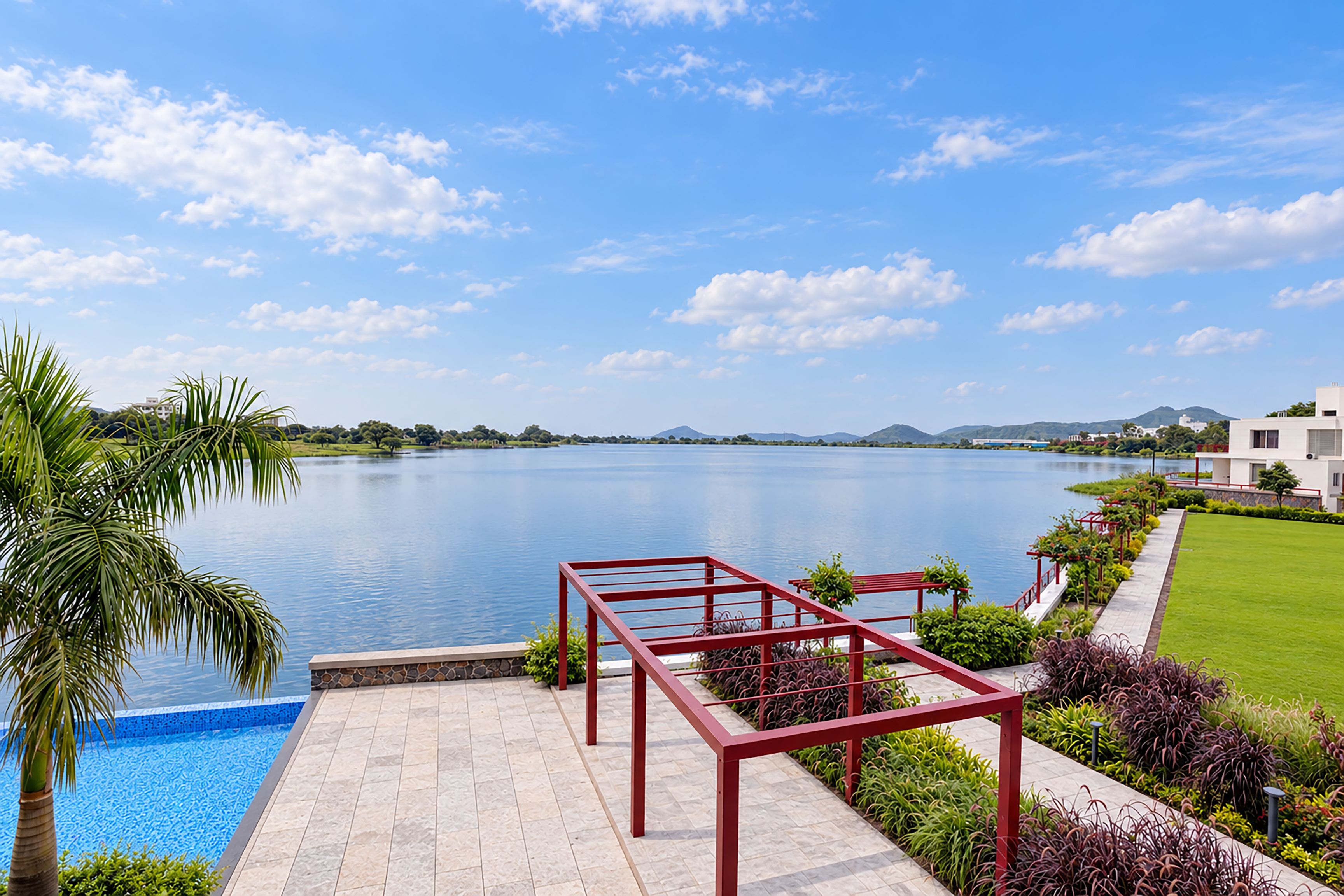A swimming pool with a red metal deck, surrounded by lush greenery and a view of a lake and distant hills.