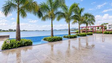 Área da piscina com vista clara da água, cercada por palmeiras e um caminho de azulejos.