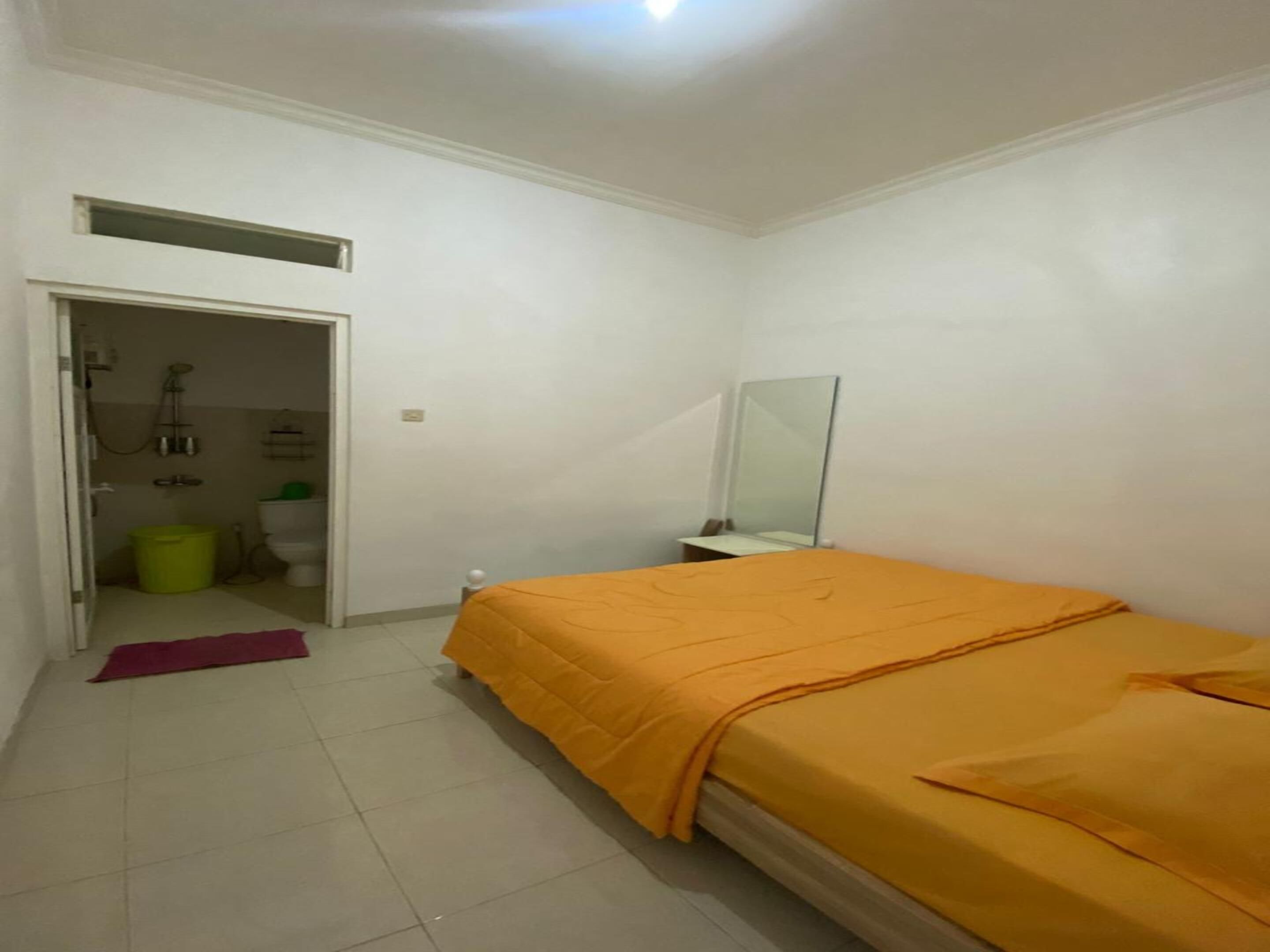 A bedroom with a bed, a mirror, a door leading to a bathroom, and a small window.